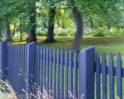 A,black,wooden,picket,fence,with,green,grass,,large,trees,